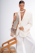 Woman in a white outfit holding a patterned handbag against a white background