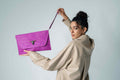 Woman holding a purple clutch bag against a plain background