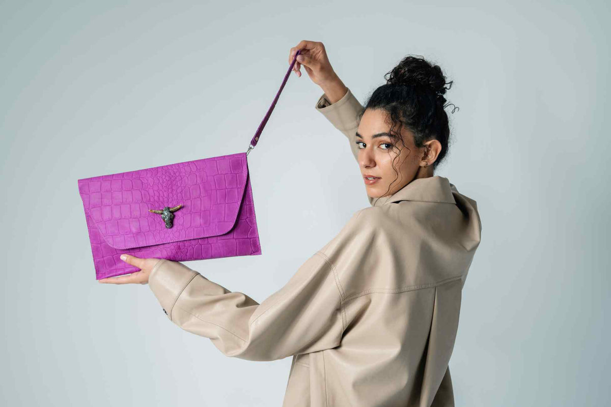 Woman holding a purple clutch bag against a plain background