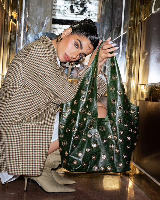 Person holding a green handbag with decorative studs in an indoor setting