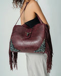 Burgundy leather handbag with fringe and sequin details on a plain background