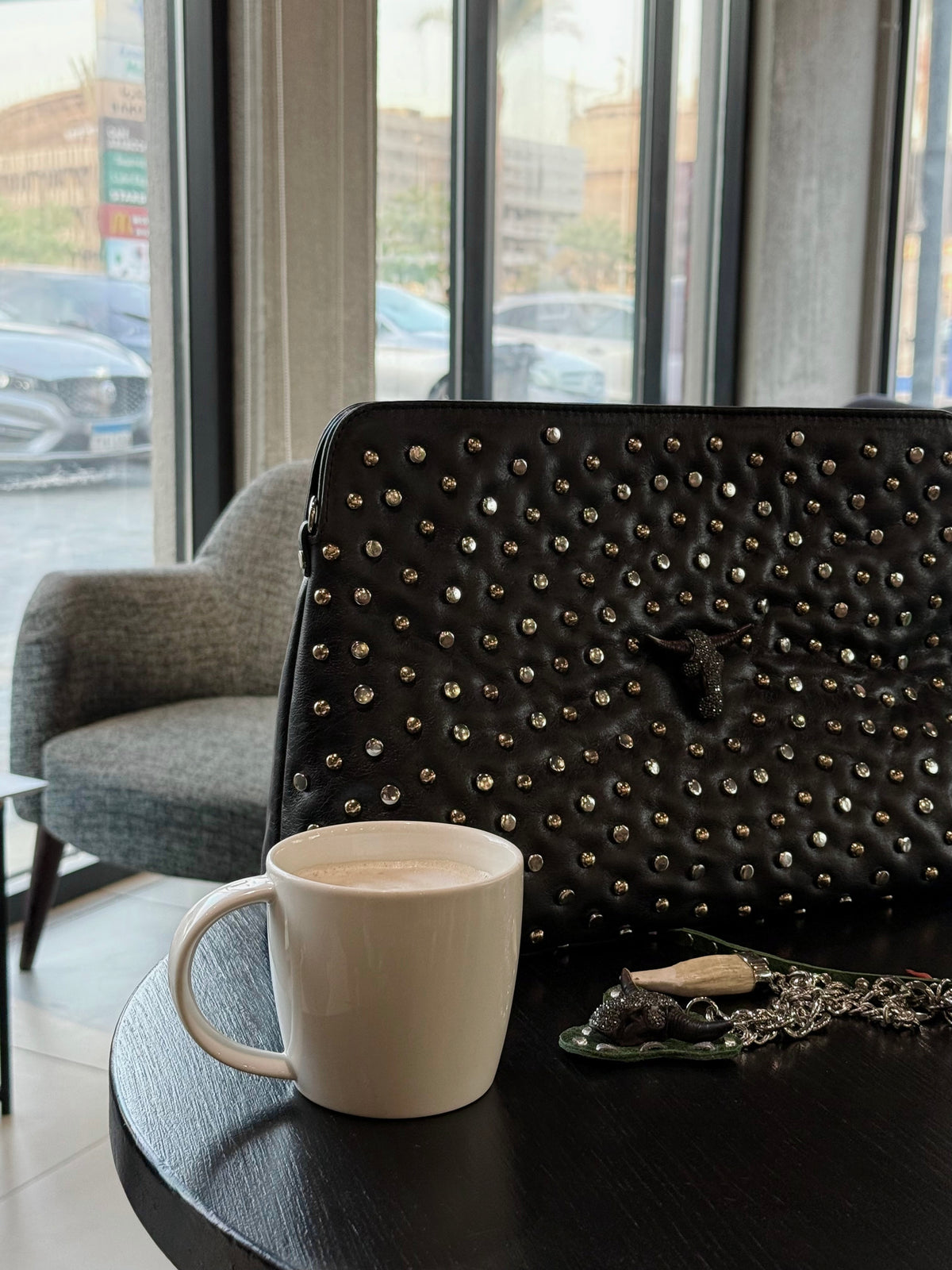 Black studded handbag on a table with a white mug in a modern interior setting.