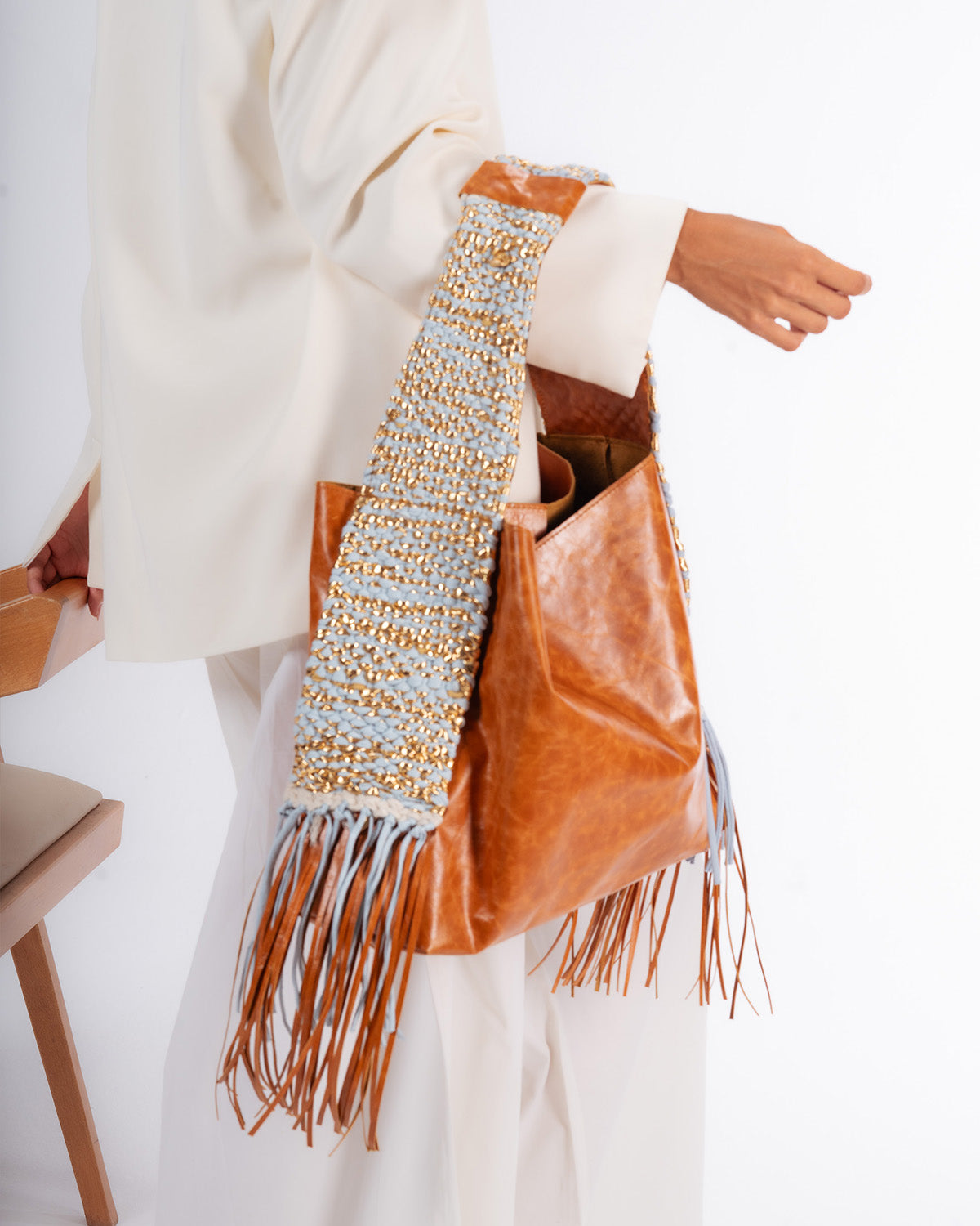 Brown leather handbag with decorative handle and fringes on a white background