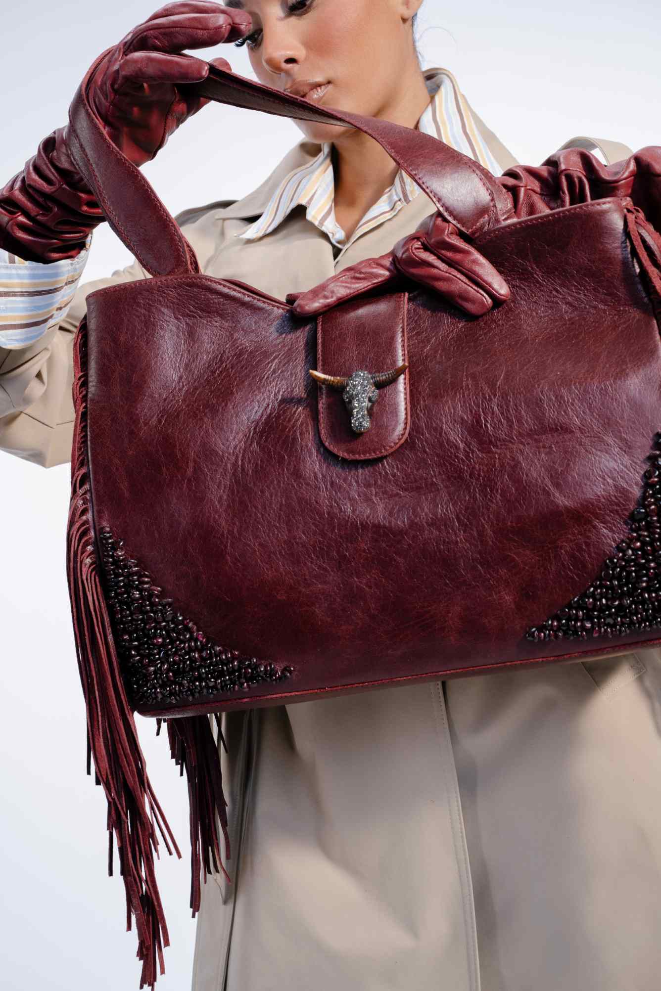 Person holding a burgundy leather handbag with fringe details on a light background