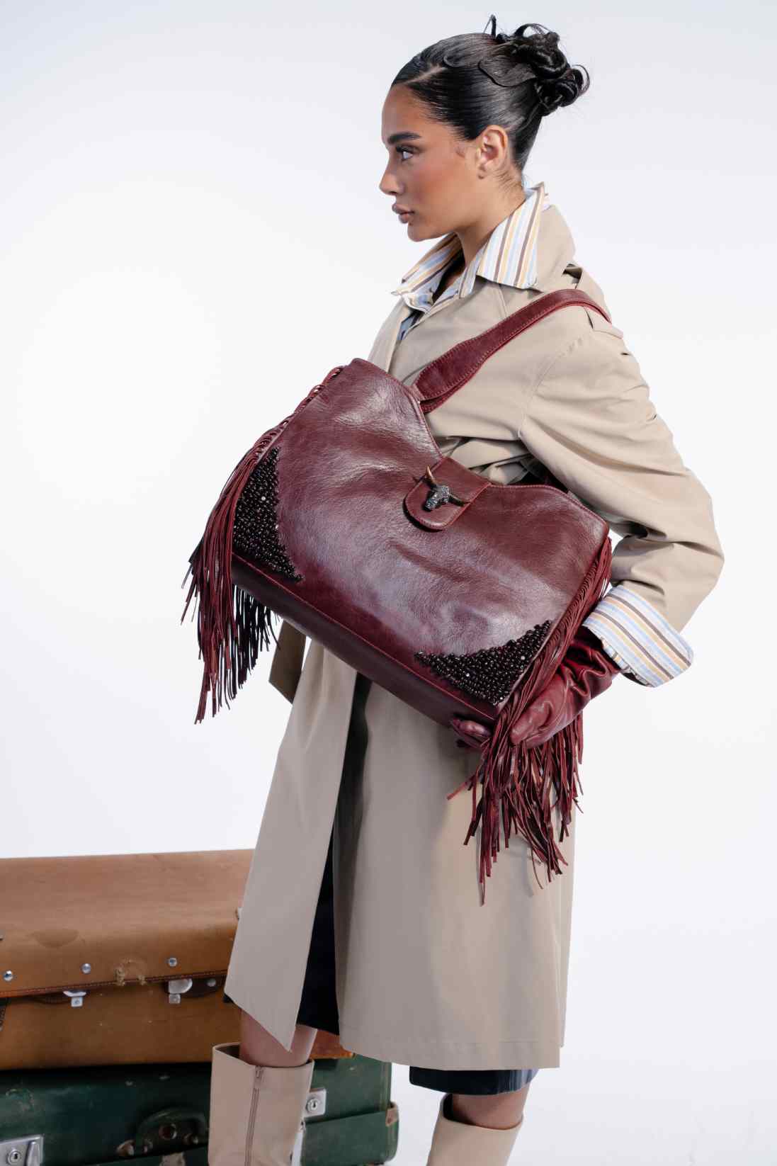 Woman holding a large brown leather bag with fringes against a white background