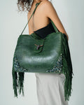 Green leather handbag with fringe and embellishments on a plain background