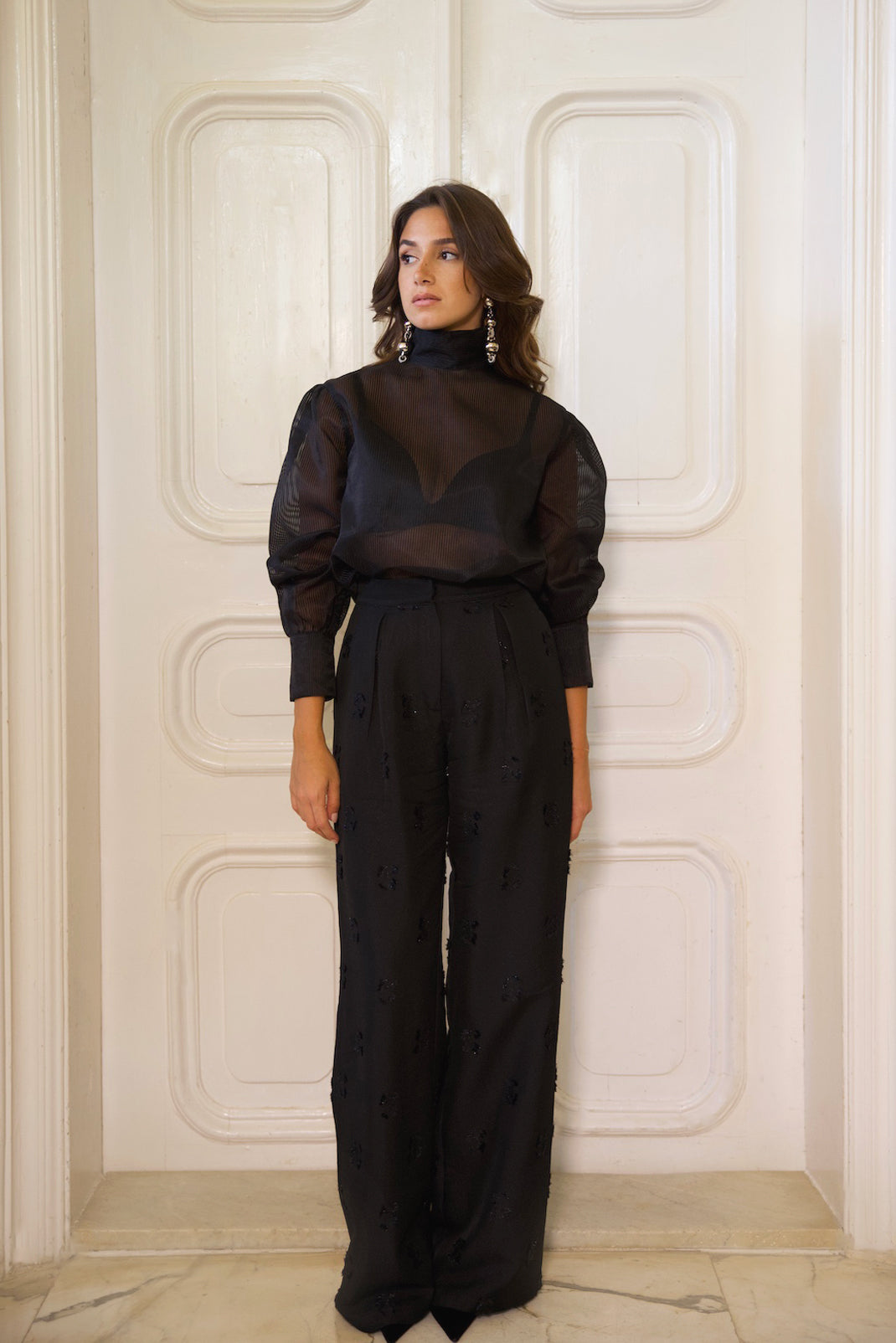 Woman wearing a black outfit against a white paneled wall cult mia