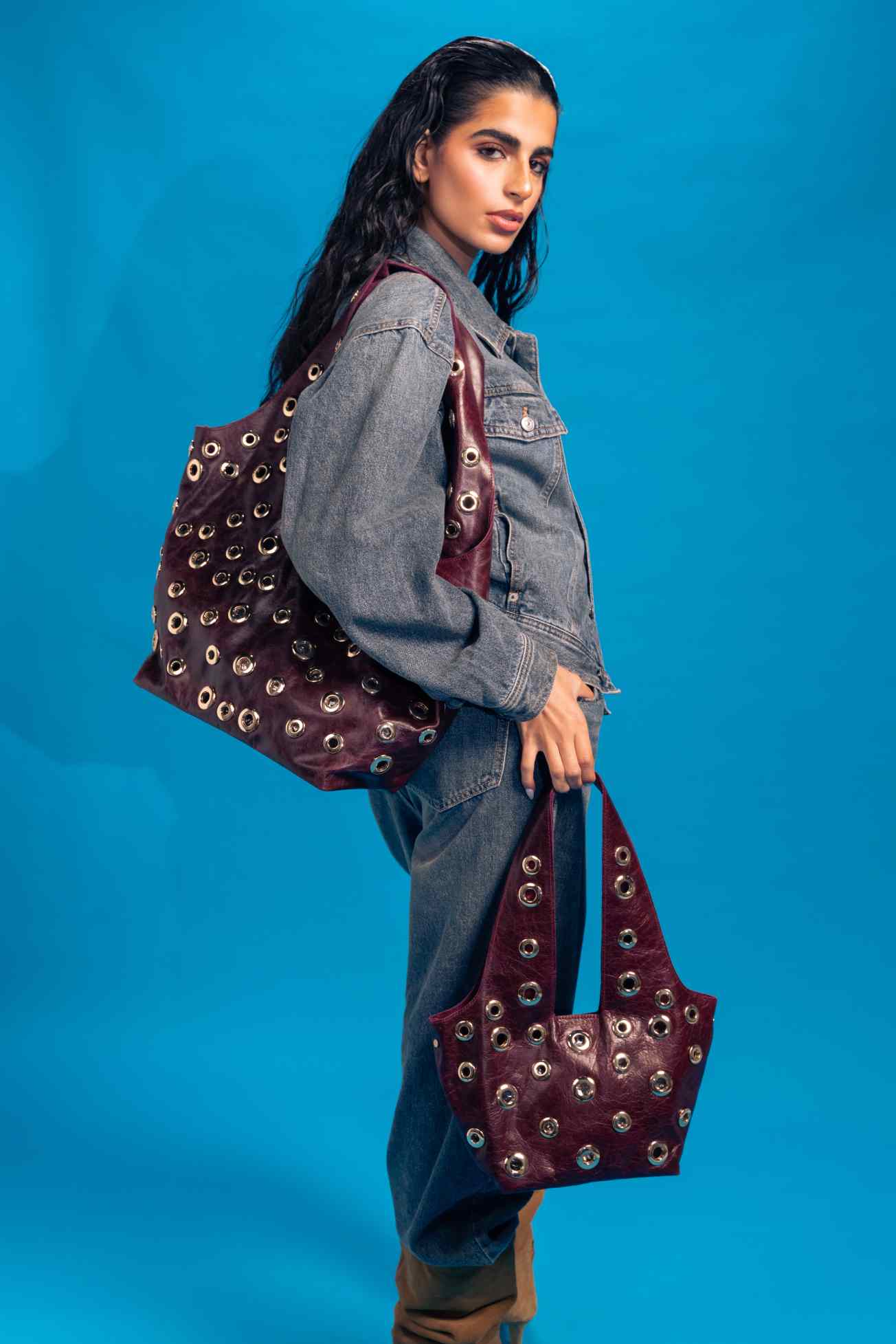 Woman holding a burgundy handbag with gold studs against a blue background