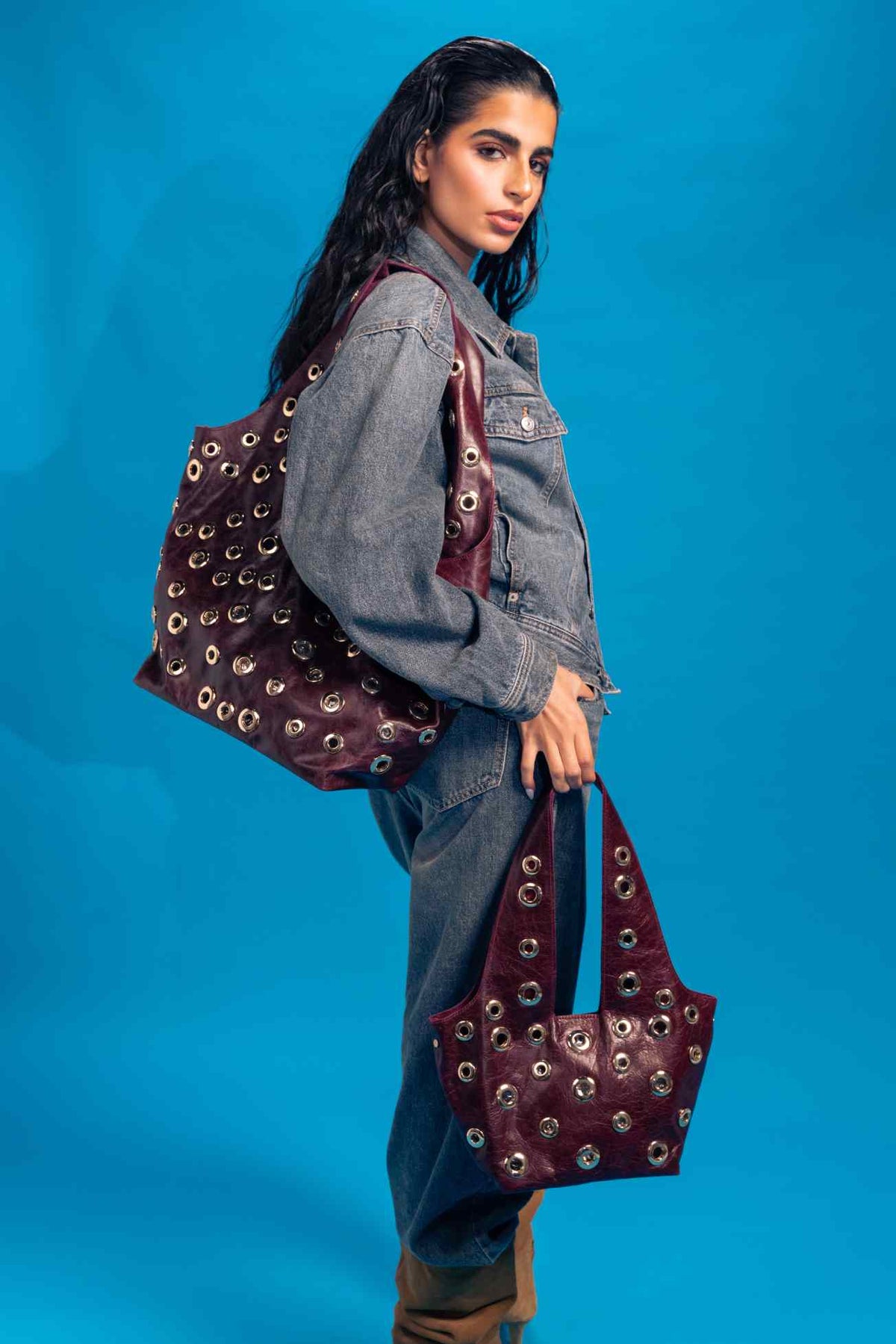 Woman holding a burgundy handbag with gold studs against a blue background