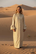 Woman in a long, light-colored coat standing in a desert landscape with sand dunes.